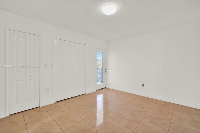 5665 W 20th Ave Unit 415, Hialeah, FL 33012 - unfurnished bedroom featuring light tile patterned flooring, baseboards, a textured ceiling, access to exterior, and multiple closets
