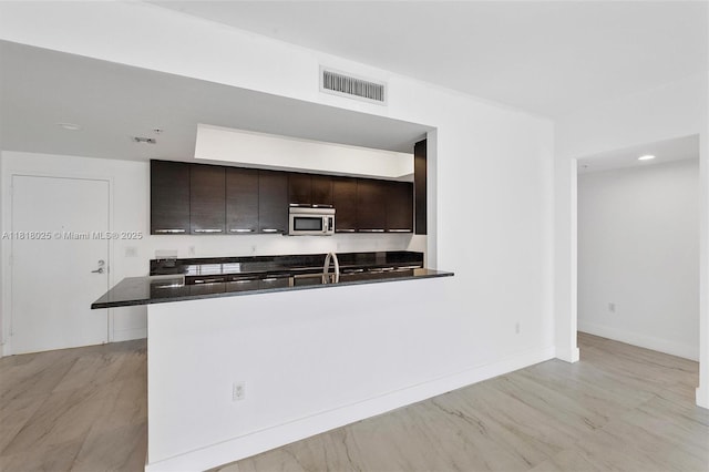 3030 NE 188th St Unit 609, Aventura, FL 33180 - kitchen featuring stainless steel microwave, dark countertops, dark brown cabinetry, and a peninsula
