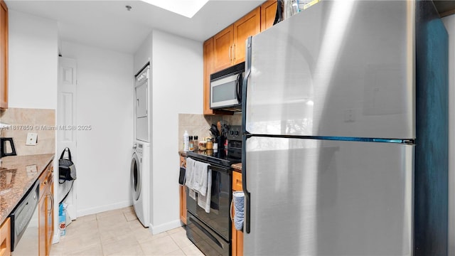 2000 N Bayshore Dr Unit 218, Miami, FL 33137 - kitchen featuring appliances with stainless steel finishes, stacked washer / dryer, brown cabinetry, stone counters, and light tile patterned flooring