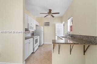 1416 N 2nd Ave N, Lake Worth, FL 33460 - kitchen featuring white appliances, a breakfast bar, a peninsula, ceiling fan, and a sink