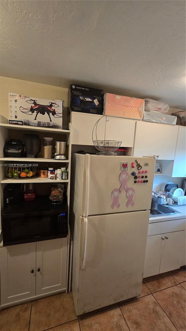 13655 NE 10th Ave Unit 108, North Miami, FL 33161 - kitchen with freestanding refrigerator, light tile patterned flooring, a textured ceiling, and white cabinets
