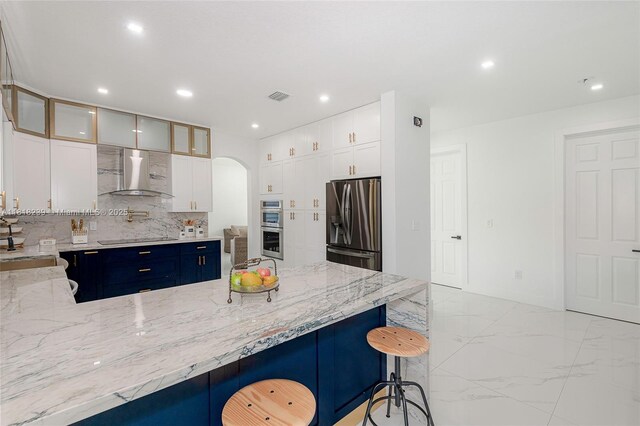 18250 SW 152nd Ave, Miami, FL 33187 - kitchen featuring appliances with stainless steel finishes, wall chimney exhaust hood, light marble finish floors, light stone counters, and arched walkways
