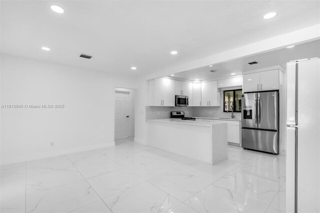 1010 NE 140th St, North Miami, FL 33161 - kitchen with appliances with stainless steel finishes, recessed lighting, white cabinetry, light countertops, and light marble finish flooring