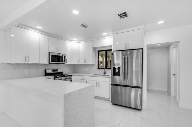 1010 NE 140th St, North Miami, FL 33161 - kitchen with appliances with stainless steel finishes, white cabinetry, recessed lighting, a peninsula, and a sink