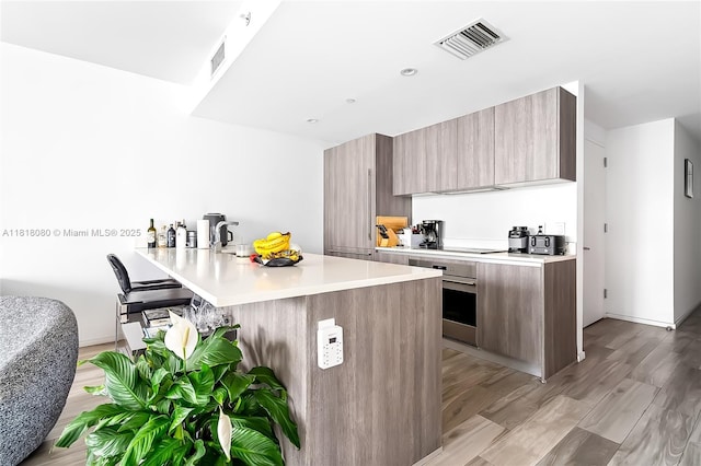 801 S Miami Ave Unit 3704, Miami, FL 33130 - kitchen with modern cabinets, stainless steel oven, a peninsula, light countertops, and light wood-type flooring