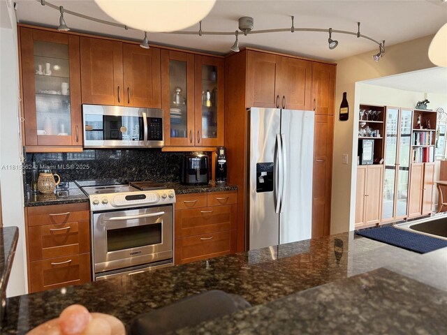 800 Parkview Dr Unit 820, Hallandale Beach, FL 33009 - kitchen featuring appliances with stainless steel finishes, brown cabinets, track lighting, tasteful backsplash, and dark stone countertops