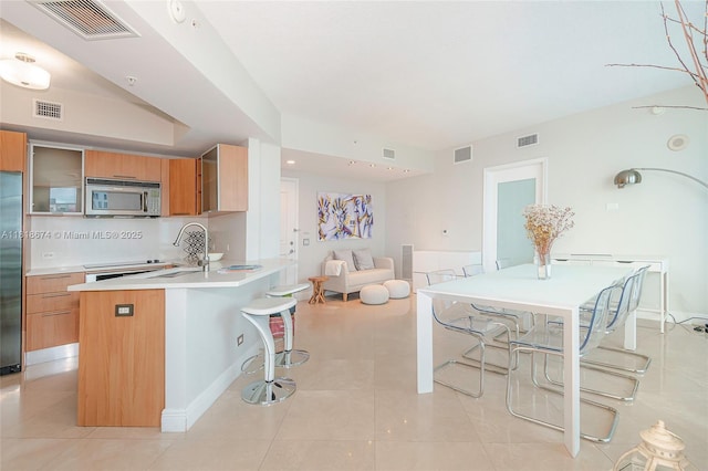 480 NE 30th St Unit 1505, Miami, FL 33137 - kitchen with appliances with stainless steel finishes, a kitchen bar, light countertops, light tile patterned floors, and brown cabinets