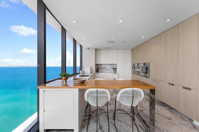 15701 Collins Ave Unit 3101, Sunny Isles Beach, FL 33160 - kitchen featuring light marble finish flooring, modern cabinets, a sink, a water view, and a breakfast bar