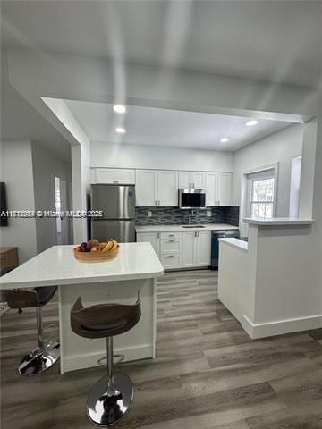 280 NE 169th St, North Miami Beach, FL 33162 - kitchen featuring appliances with stainless steel finishes, white cabinetry, a breakfast bar, wood finished floors, and recessed lighting