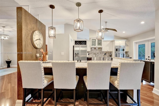 18366 Lake Bend Dr, Jupiter, FL 33458 - kitchen with appliances with stainless steel finishes, vaulted ceiling, decorative backsplash, glass insert cabinets, and white cabinetry