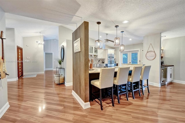 18366 Lake Bend Dr, Jupiter, FL 33458 - kitchen featuring beverage cooler, lofted ceiling, a kitchen bar, light wood-type flooring, and stainless steel double oven