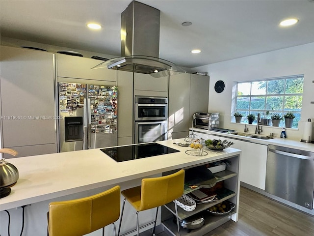 7650 SW 78th Ct, Miami, FL 33143 - kitchen featuring appliances with stainless steel finishes, island range hood, light countertops, wood finished floors, and modern cabinets