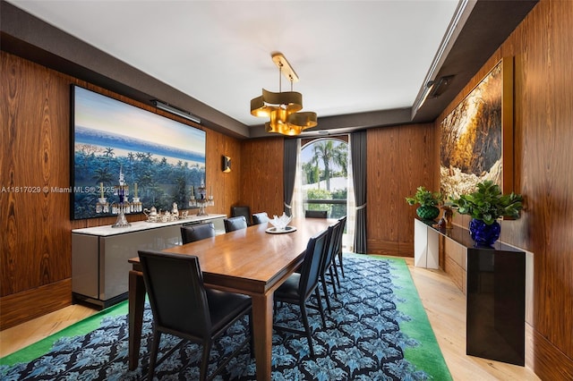 dining space with a chandelier, wood walls, and light wood-style flooring