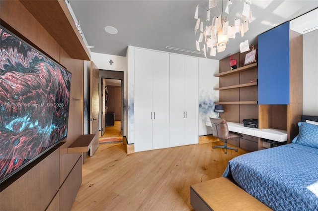 bedroom with light wood-style floors, built in study area, a closet, and a chandelier