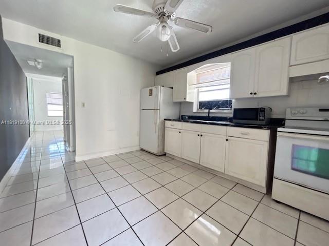 515 SW 3rd St Unit 12, Miami, FL 33130 - kitchen with white appliances, light tile patterned flooring, dark countertops, ceiling fan, and white cabinetry