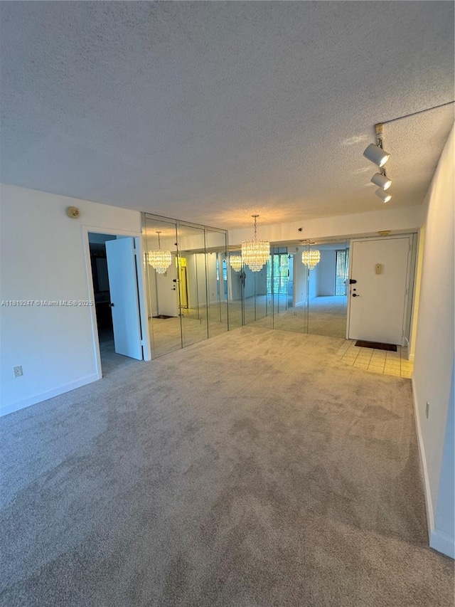 1100 Saint Charles Pl Unit 203, Pembroke Pines, FL 33026 - unfurnished living room featuring a textured ceiling, light carpet, rail lighting, a chandelier, and baseboards