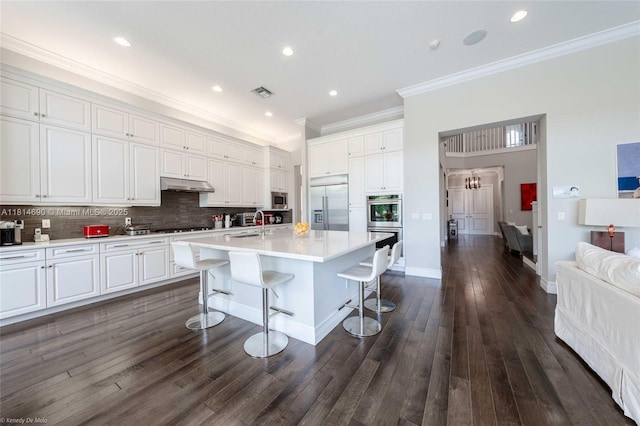 9368 Eden Roc Ct, Delray Beach, FL 33446 - kitchen featuring built in appliances, under cabinet range hood, ornamental molding, a breakfast bar, and dark wood finished floors