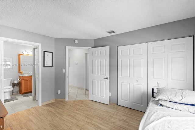 7182 Burgess Dr, Lake Worth, FL 33467 - bedroom featuring light wood finished floors, a closet, a textured ceiling, connected bathroom, and a sink