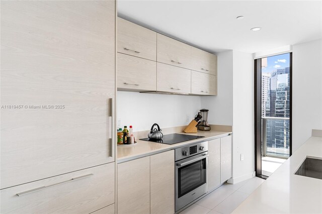 1300 S Miami Ave Unit 2305, Miami, FL 33130 - kitchen featuring oven, light countertops, black electric cooktop, a wall of windows, and cream cabinetry