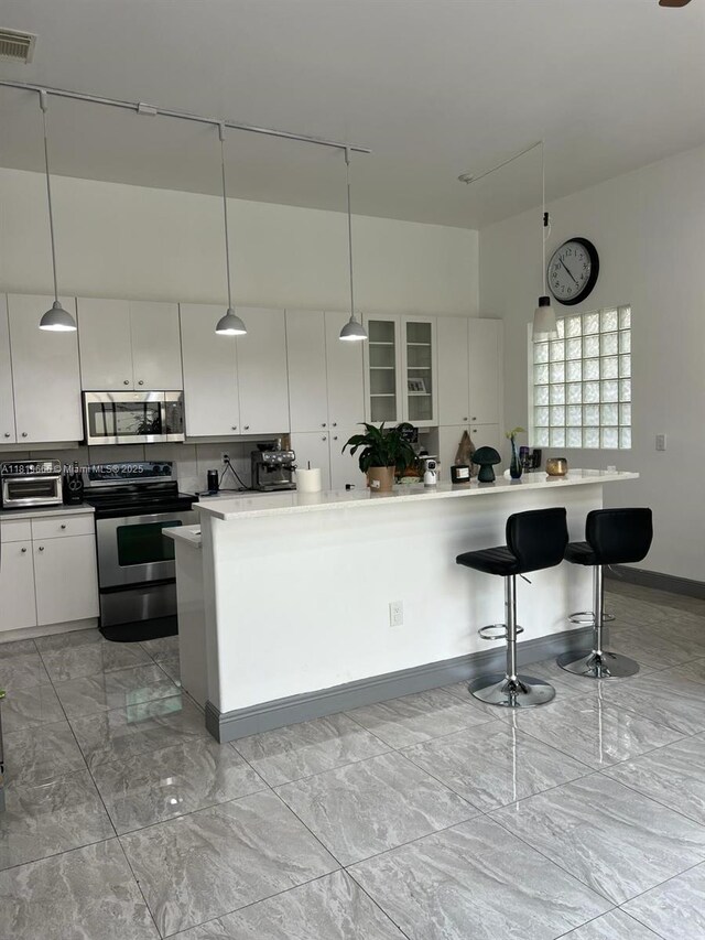 1120 Papaya St, Hollywood, FL 33019 - kitchen with appliances with stainless steel finishes, white cabinets, hanging light fixtures, a breakfast bar area, and light marble finish floors