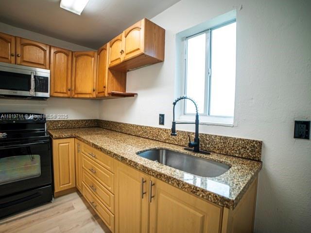 412 Columbus Pkwy, Hollywood, FL 33021 - kitchen featuring black range with electric stovetop, stainless steel microwave, a sink, dark stone counters, and light wood finished floors
