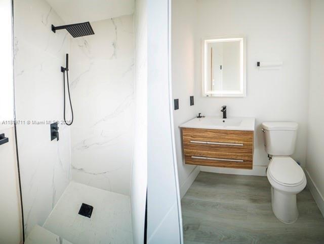 412 Columbus Pkwy, Hollywood, FL 33021 - bathroom featuring vanity, a marble finish shower, toilet, wood finished floors, and baseboards
