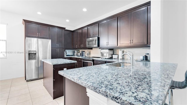 11530 SW 13th Ct, Pembroke Pines, FL 33025 - kitchen featuring stainless steel appliances, a sink, light stone countertops, a center island, and dark brown cabinets