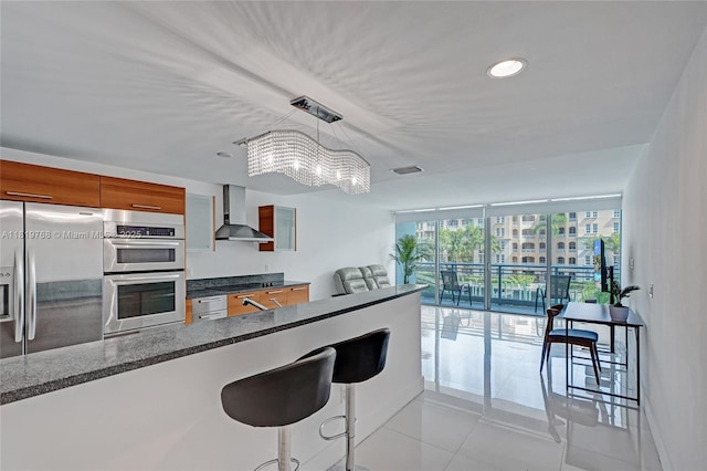 2950 NE 188th St Unit 225, Aventura, FL 33180 - kitchen featuring wall chimney range hood, stainless steel appliances, a chandelier, brown cabinetry, and light tile patterned floors