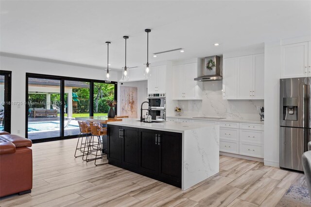 7570 SW 60th St, Miami, FL 33143 - kitchen featuring stainless steel appliances, wall chimney exhaust hood, an island with sink, white cabinetry, and light wood-style flooring