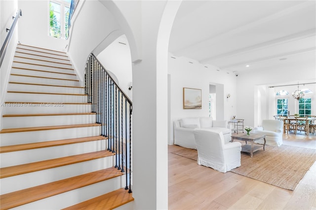 stairs with wood finished floors, arched walkways, and a chandelier