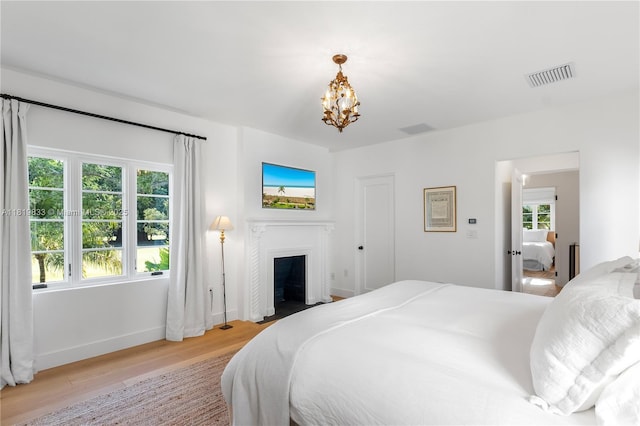 bedroom with light wood-style flooring, a chandelier, a fireplace, and baseboards