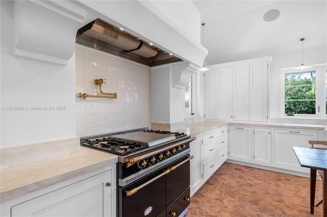 kitchen with range with two ovens, wall chimney range hood, white cabinetry, and backsplash