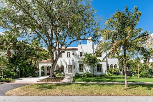 mediterranean / spanish-style home featuring asphalt driveway, a front yard, a tiled roof, a chimney, and stucco siding
