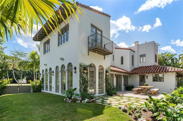 back of house with a balcony, a patio, stucco siding, and a tiled roof