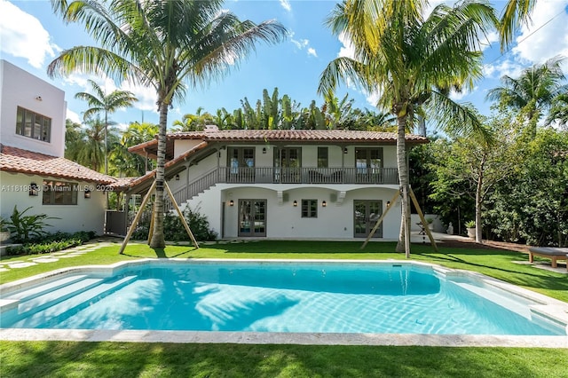 rear view of property with french doors, stucco siding, a lawn, an outdoor pool, and a tiled roof
