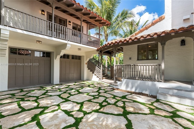 covered porch featuring a garage, a balcony, and stairway
