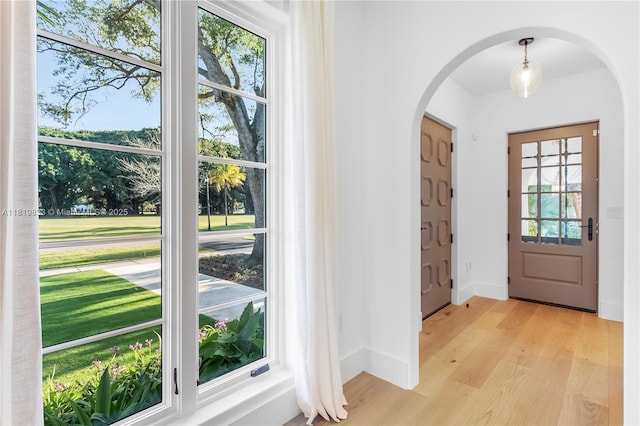 entrance foyer featuring arched walkways, light wood-style flooring, and baseboards