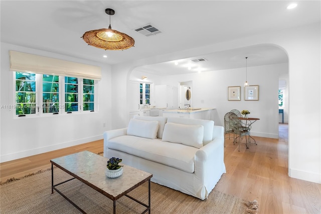 living room featuring arched walkways, light wood-type flooring, baseboards, and recessed lighting