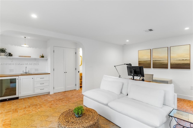 living room with beverage cooler, bar with sink, recessed lighting, and arched walkways