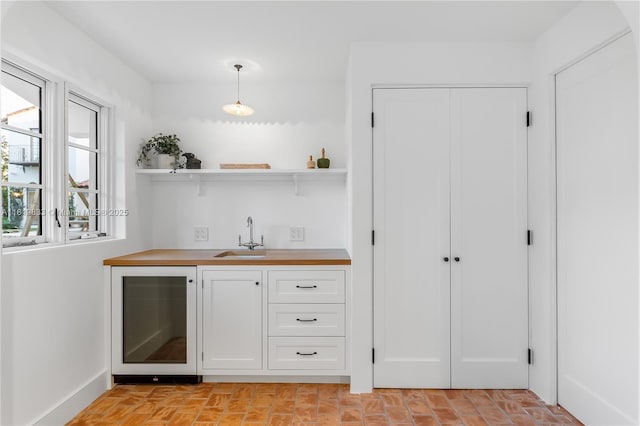 indoor wet bar featuring wine cooler, pendant lighting, and baseboards