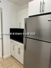 8888 Collins Ave Unit 318, Surfside, FL 33154 - kitchen with freestanding refrigerator, light tile patterned floors, white cabinetry, and baseboards