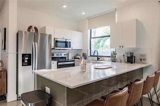 3645 SW 3rd St, Miami, FL 33135 - kitchen with appliances with stainless steel finishes, a peninsula, white cabinets, light stone countertops, and a kitchen bar