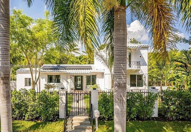 659 NE 73rd St, Miami, FL 33138 - view of front facade with a gate, a balcony, a fenced front yard, solar panels, and stucco siding