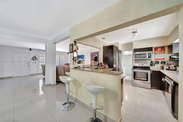 14925 NE 7th Ave, Miami, FL 33161 - kitchen with appliances with stainless steel finishes, tasteful backsplash, light tile patterned flooring, light stone countertops, and a kitchen breakfast bar