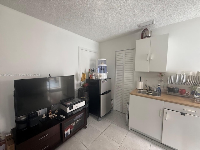 2413 W 73rd Pl, Hialeah, FL 33016 - kitchen featuring freestanding refrigerator, white cabinetry, a textured ceiling, light tile patterned floors, and light countertops