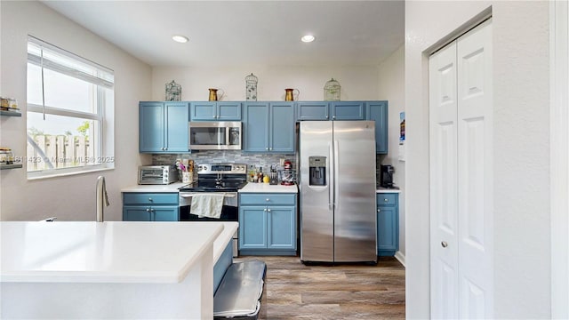 2389 NE 4th St, Homestead, FL 33033 - kitchen with appliances with stainless steel finishes, blue cabinetry, wood finished floors, light countertops, and tasteful backsplash