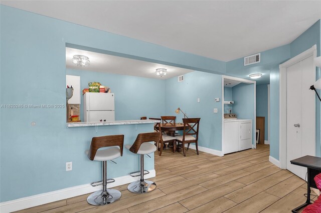 251 W Palm Cir W Unit 207, Pembroke Pines, FL 33025 - kitchen with freestanding refrigerator, washer / dryer, light wood finished floors, a breakfast bar, and light countertops