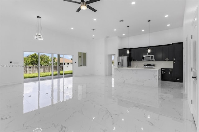 3512 2nd St W, Lehigh Acres, FL 33971 - kitchen featuring stainless steel appliances, dark cabinetry, a high ceiling, open floor plan, and light marble finish flooring
