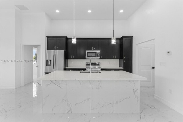 3512 2nd St W, Lehigh Acres, FL 33971 - kitchen with stainless steel appliances, dark cabinetry, light marble finish floors, an island with sink, and pendant lighting