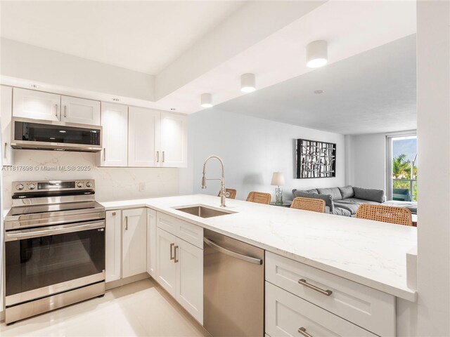 5701 Collins Ave Unit 307, Miami Beach, FL 33140 - kitchen with stainless steel appliances, light stone countertops, a peninsula, open floor plan, and white cabinetry